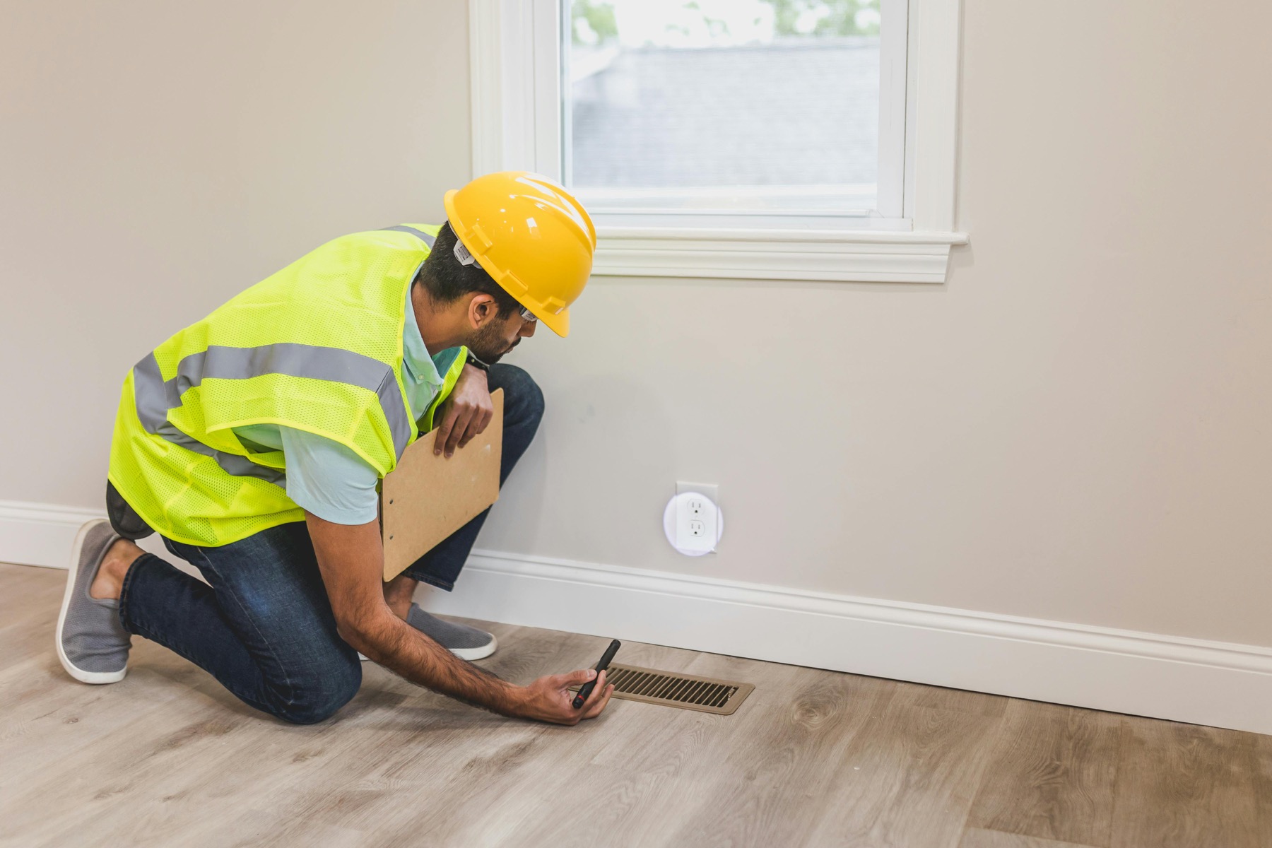 Home inspector checking moisture near a wall vent inside a Long Island home